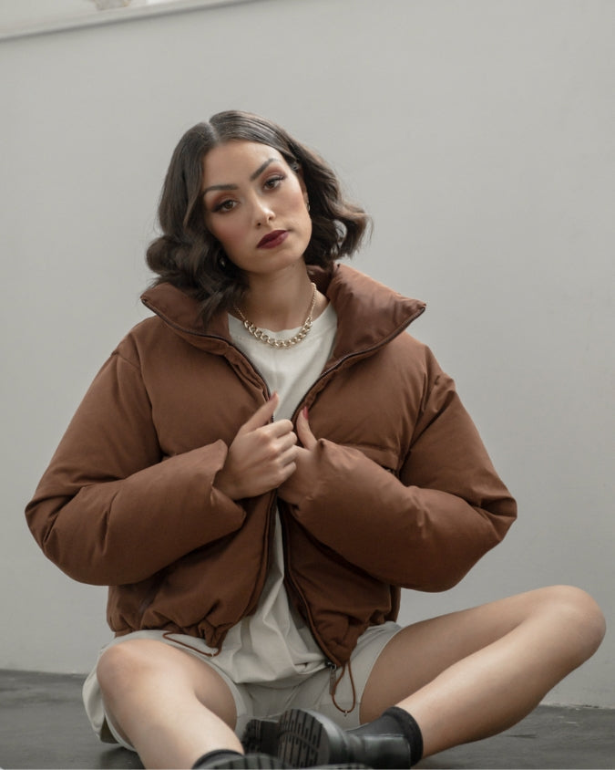 Cropped chocolate brown puffer jacket worn my female model sitting down